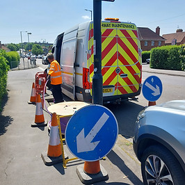 A cabling employee doing work near a van and roadworks signs.